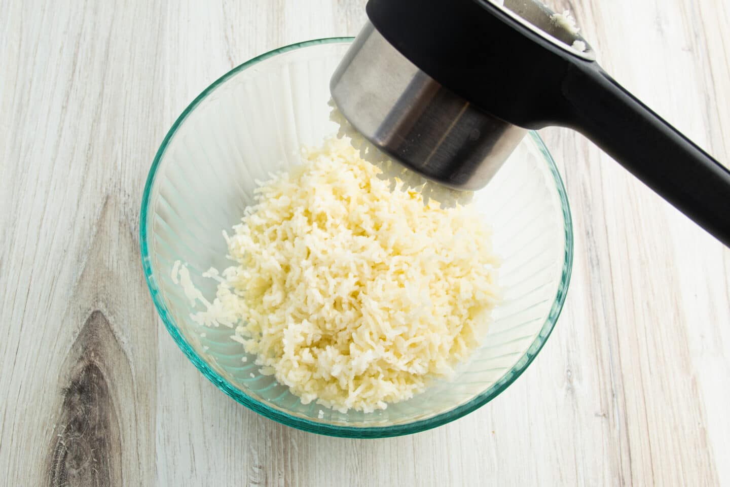 Cooked potatoes being mashed thru potato ricer.