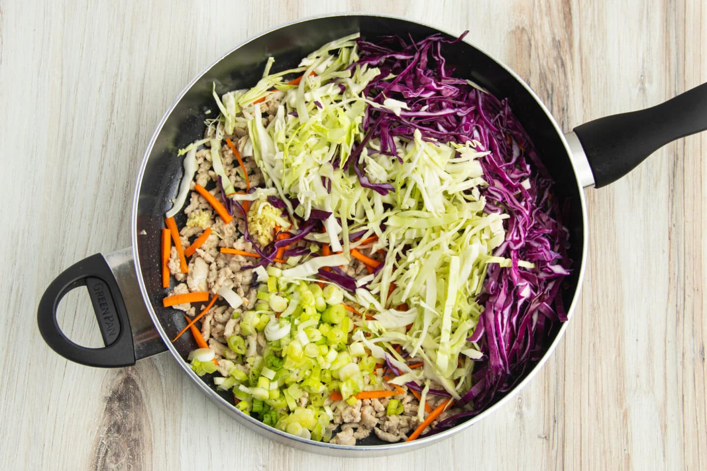 Picture of a skillet with added cabbage, carrots and green onions.