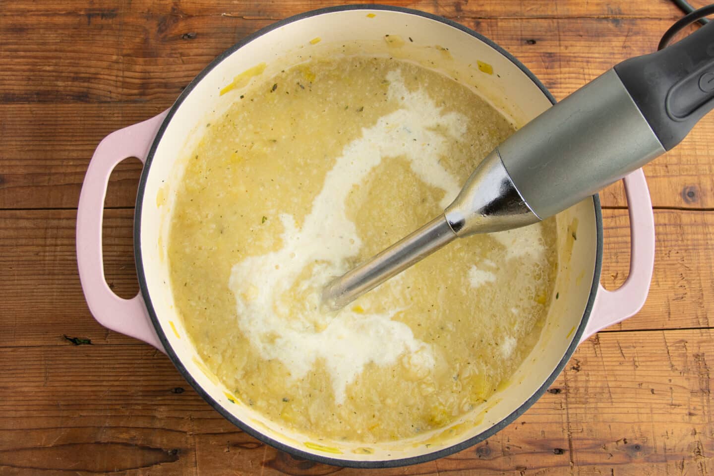 This is a picture of a big pot with the soup being blended with an immersion blender.