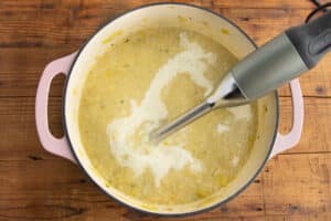 This is a picture of a big pot with the soup being blended with an immersion blender.