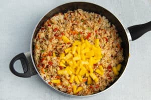 Picture of skillet with fried rice with soy sauce and pineapple added.