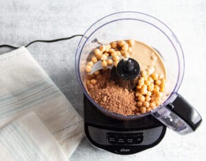 Picture of a food processor with all ingredients inside to make chocolate hummus.