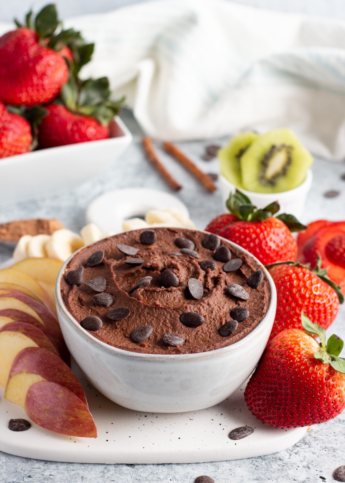 dark chocolate hummus picture in a bowl with fruits around including apple, strawberries, banana and kiwi.