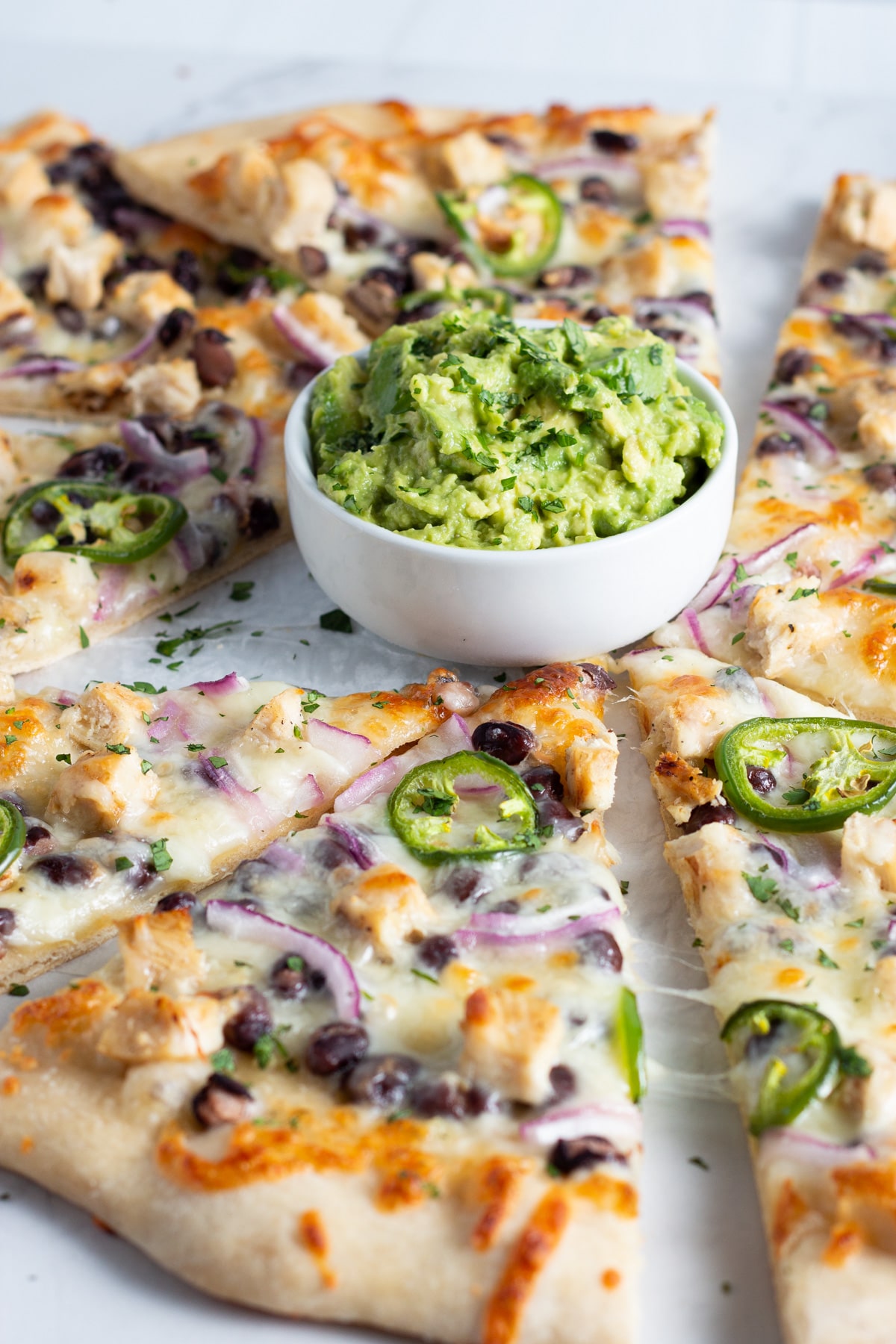 picture of pizza with chicken ,black beans, cheese, onion and jalapeño with a little bowl of smashed avocado.