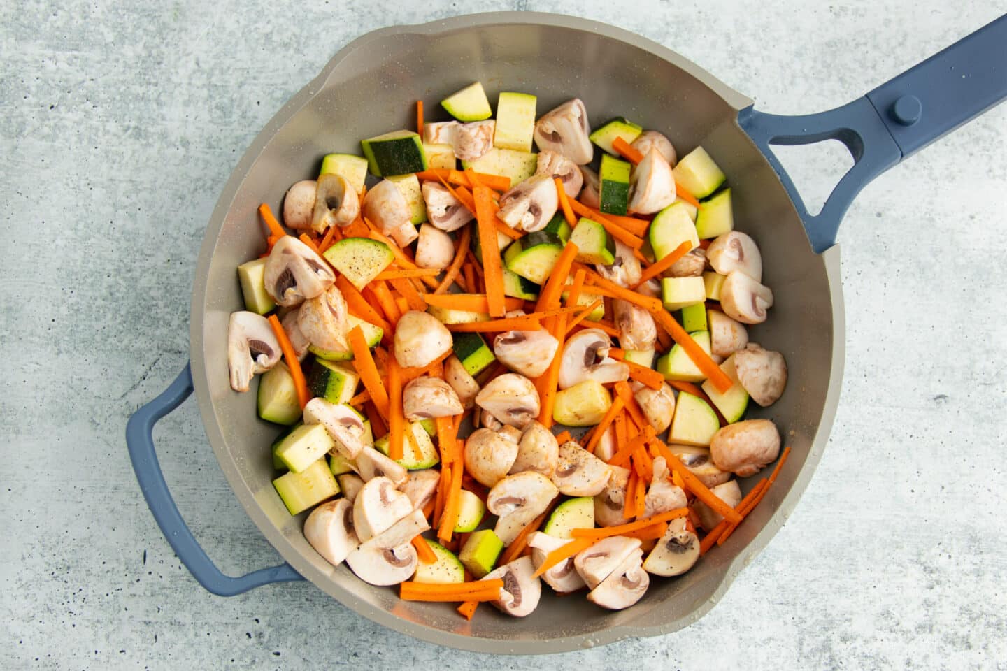 Picture of raw mushrooms, zucchini and carrots added to skillet to cook. 