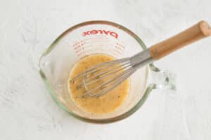 Picture of measuring cup with vinaigrette and whisk.
