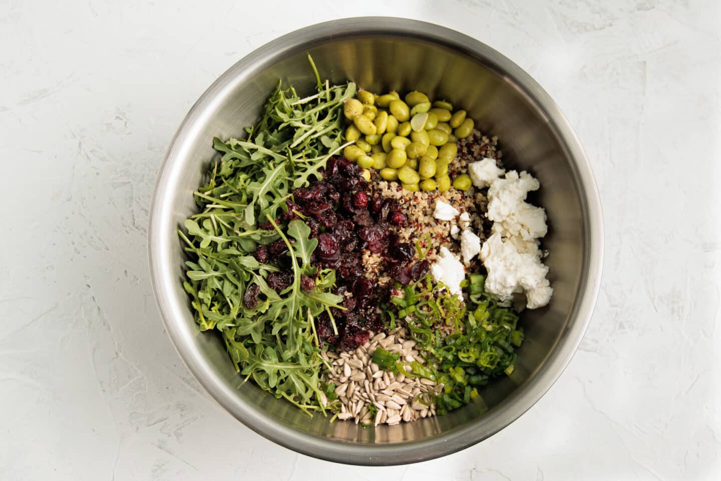 Bowl with all ingredients of quinoa arugula salad before being tossed together.