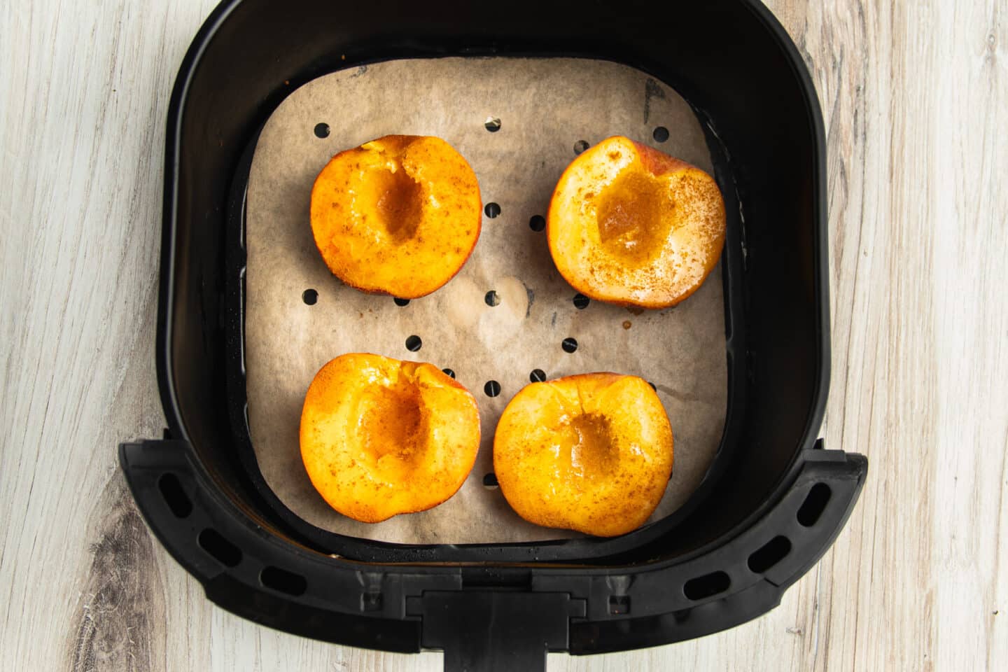 Picture of air fryer with parchment paper liner and peaches halves on top.