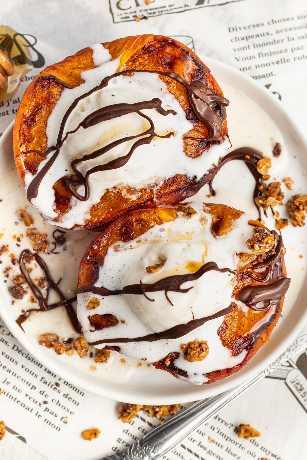 Picture of air fryer peaches topped with ice cream, honey, chocolate drizzle and granola.