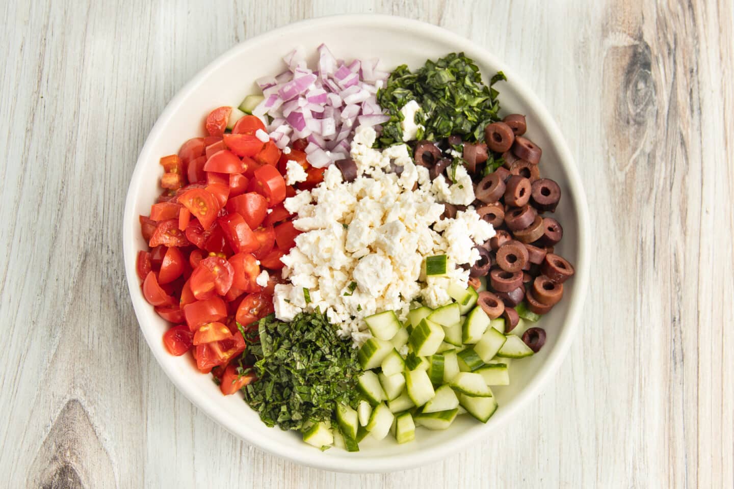 Picture of all veggies, feta and herbs in a white bowl.