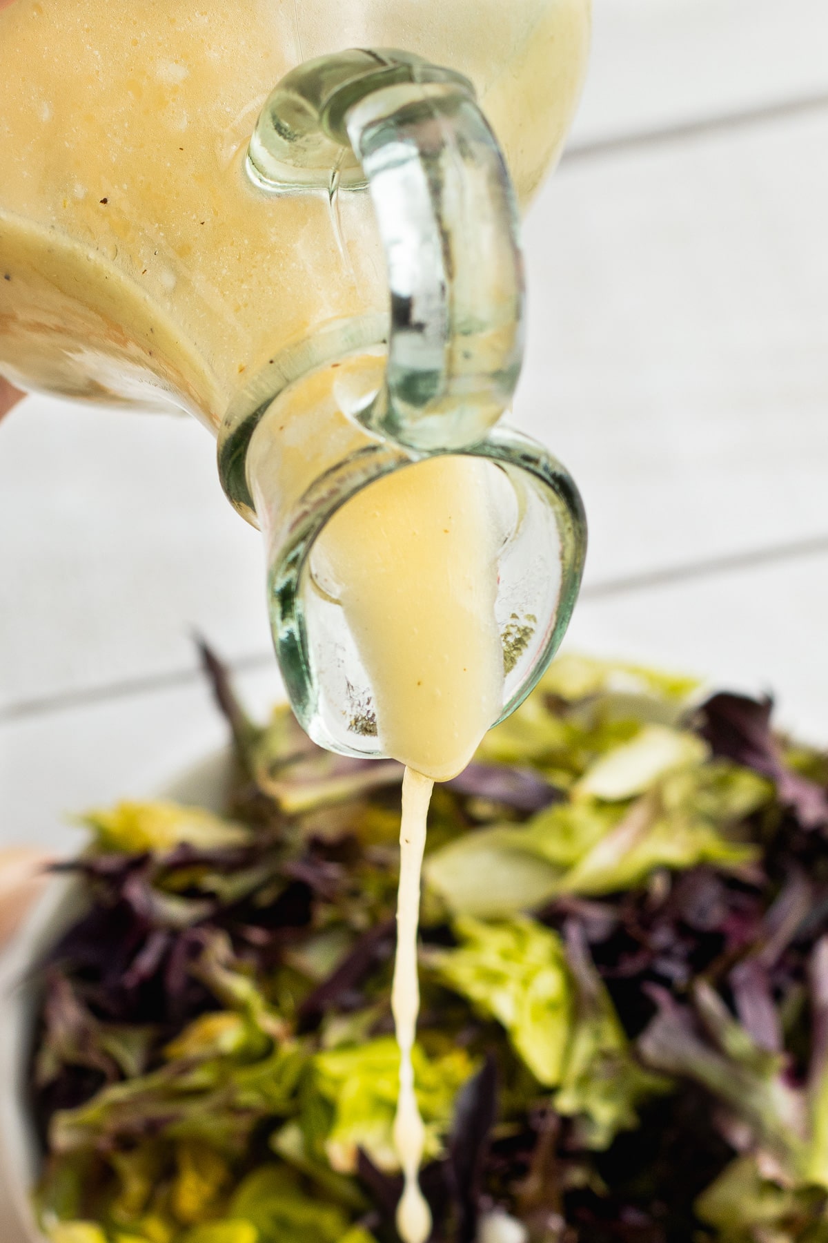 Picture of homemade vinaigrette being poured over a salad. 