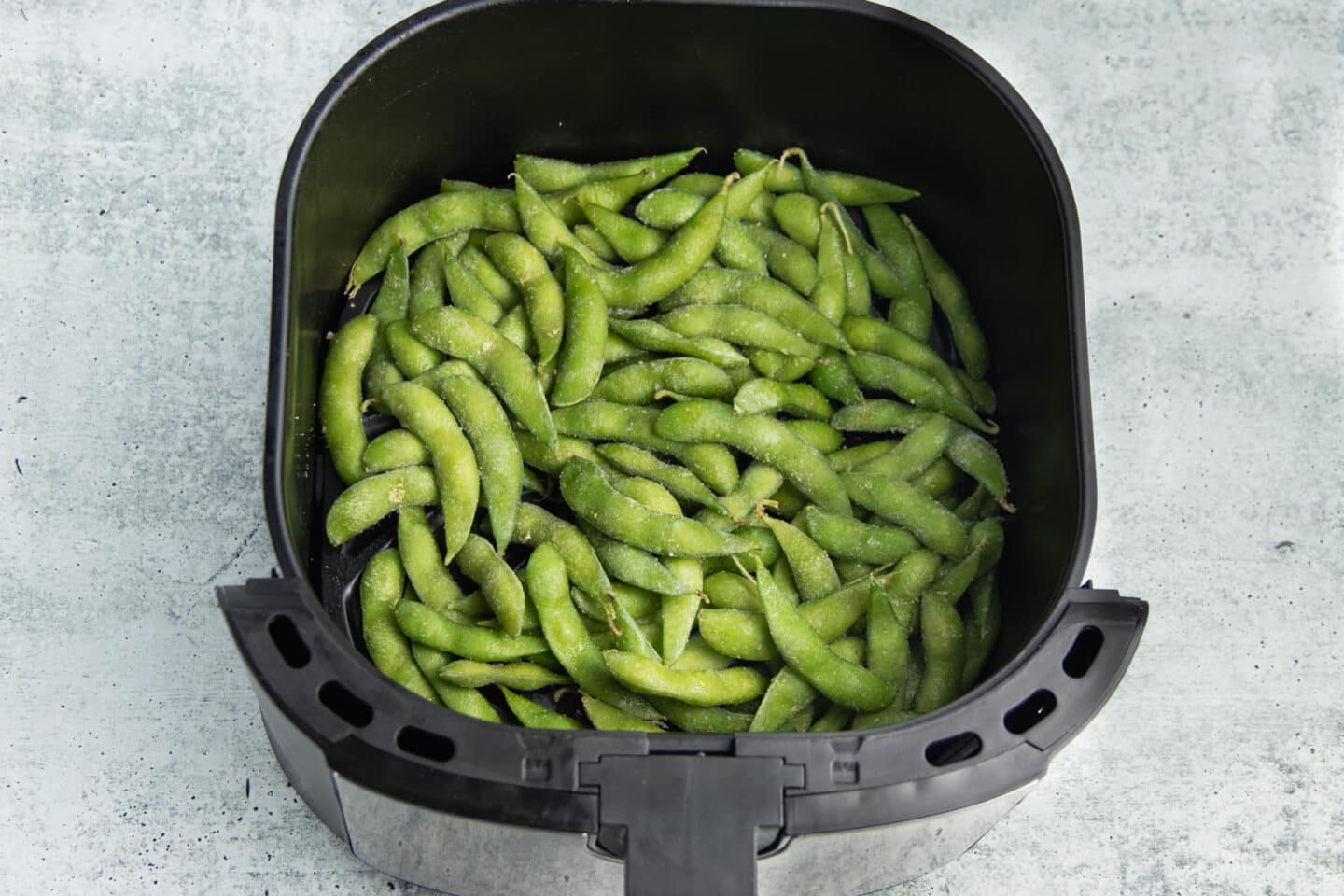 This is picture of edamame in an air fryer basket.