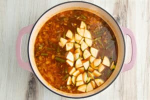 Picture of large pot with soup and potatoes, zucchini and beans added.