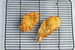 This is a picture of a chicken cutlets resting on a metal rack.