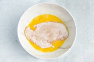 This is a picture of a chicken cutlet being dipped in egg wash.