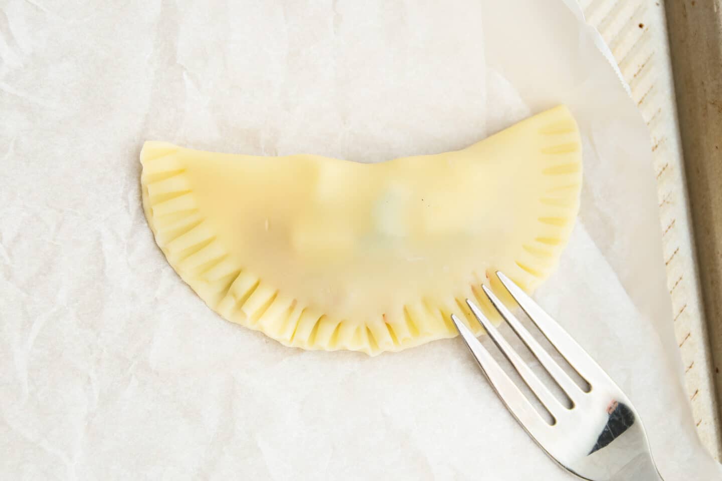 This is a picture of an empanada being sealed with a fork.