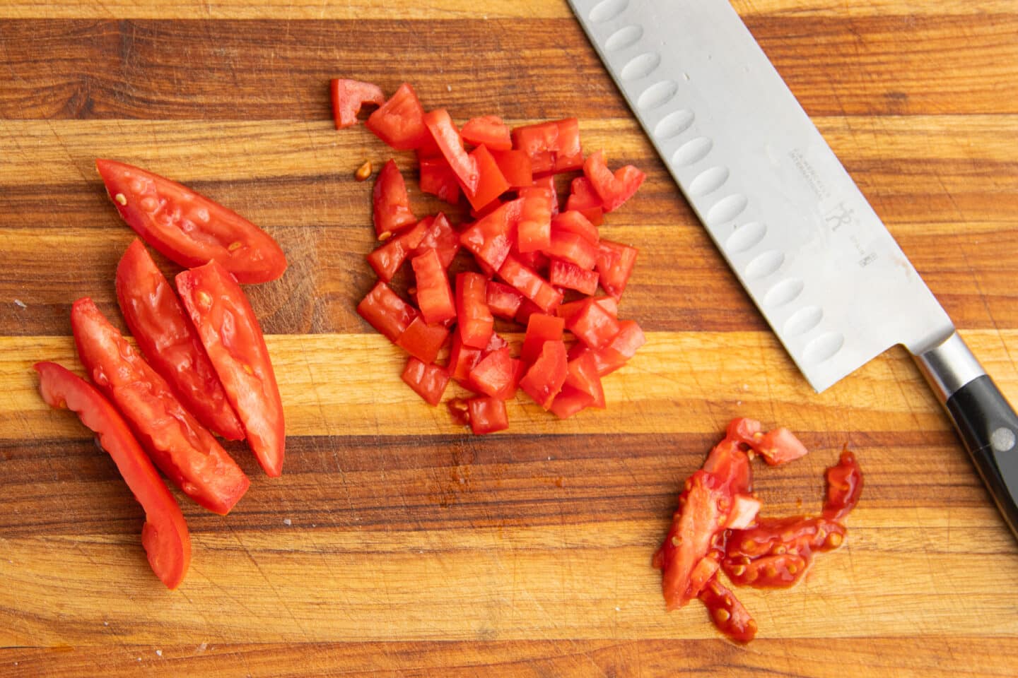 This is a picture of a cutting board and diced tomatoes with a knife. 