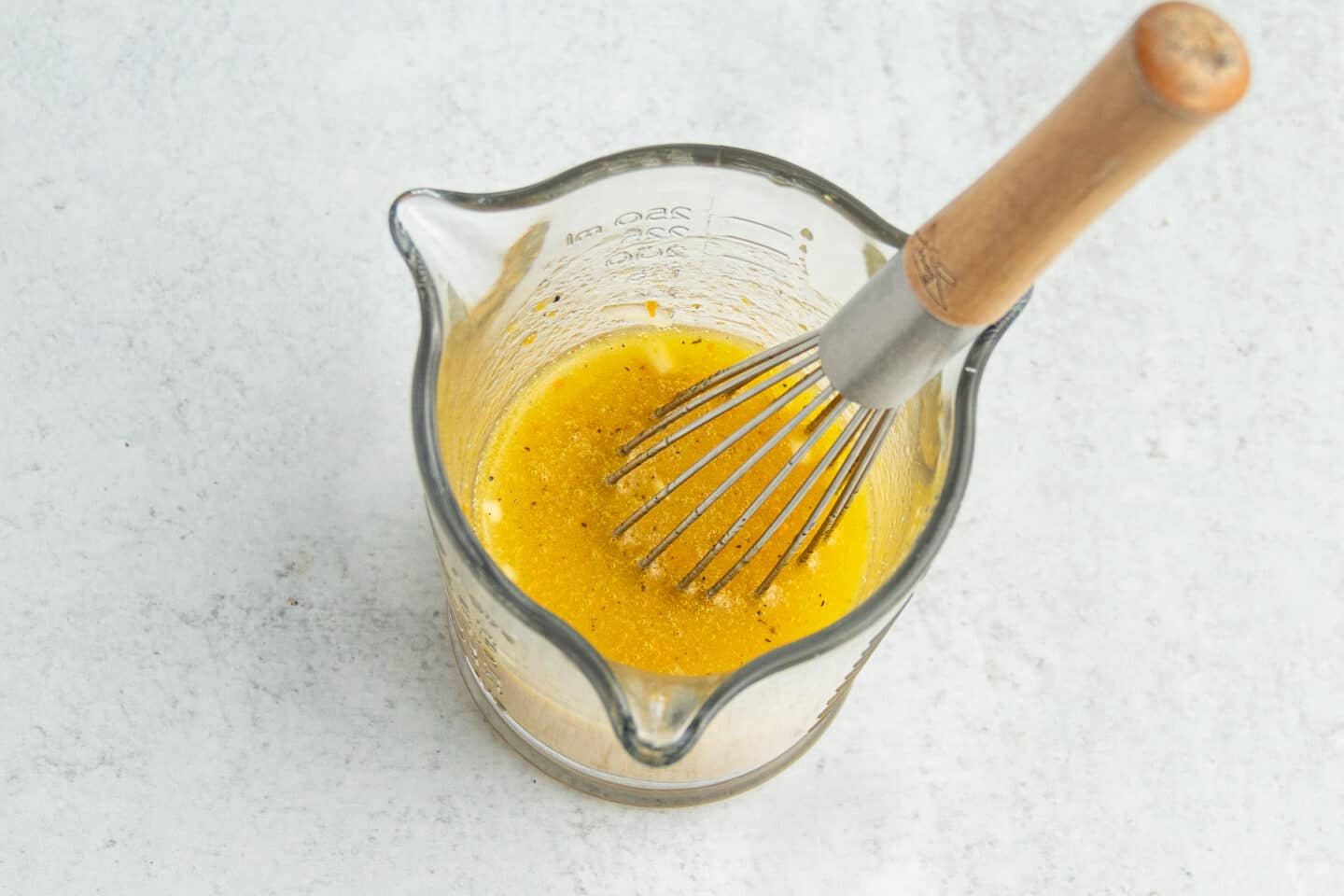 This is a picture of a cup with the orange vinaigrette and a whisk. 