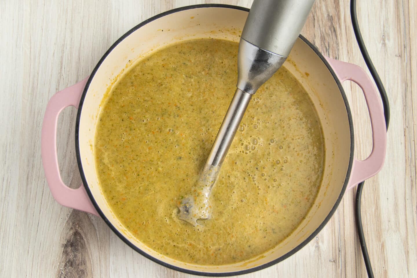 This is a picture of a pot with with the soup being blended with an immersion blender.