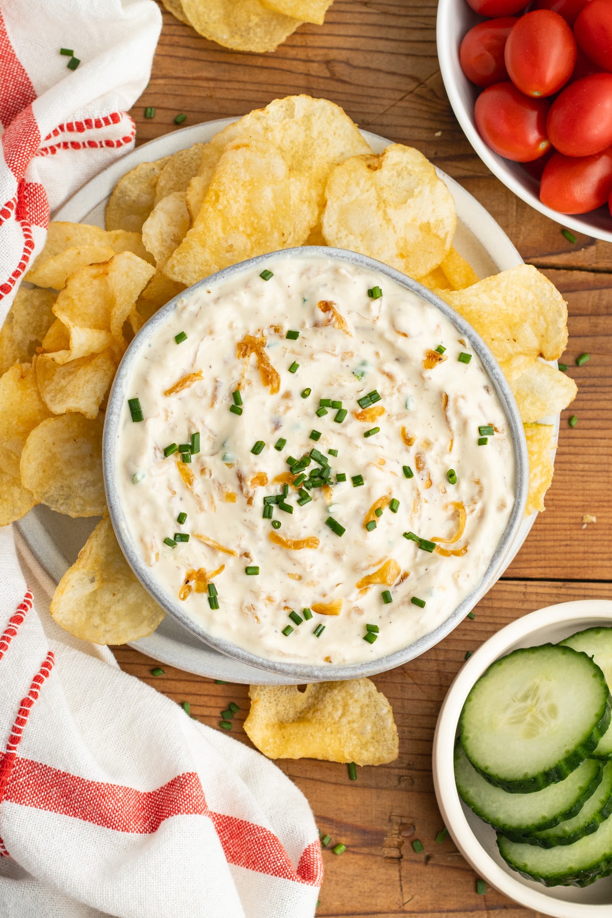 This is a picture of a bowl with the onion dip, chips, tomatoes and cucumber.