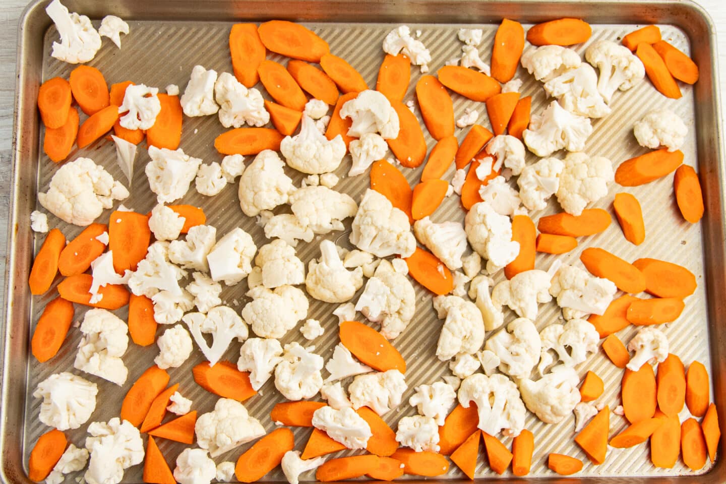 This is a picture of a baking tray with raw carrots and cauliflower.