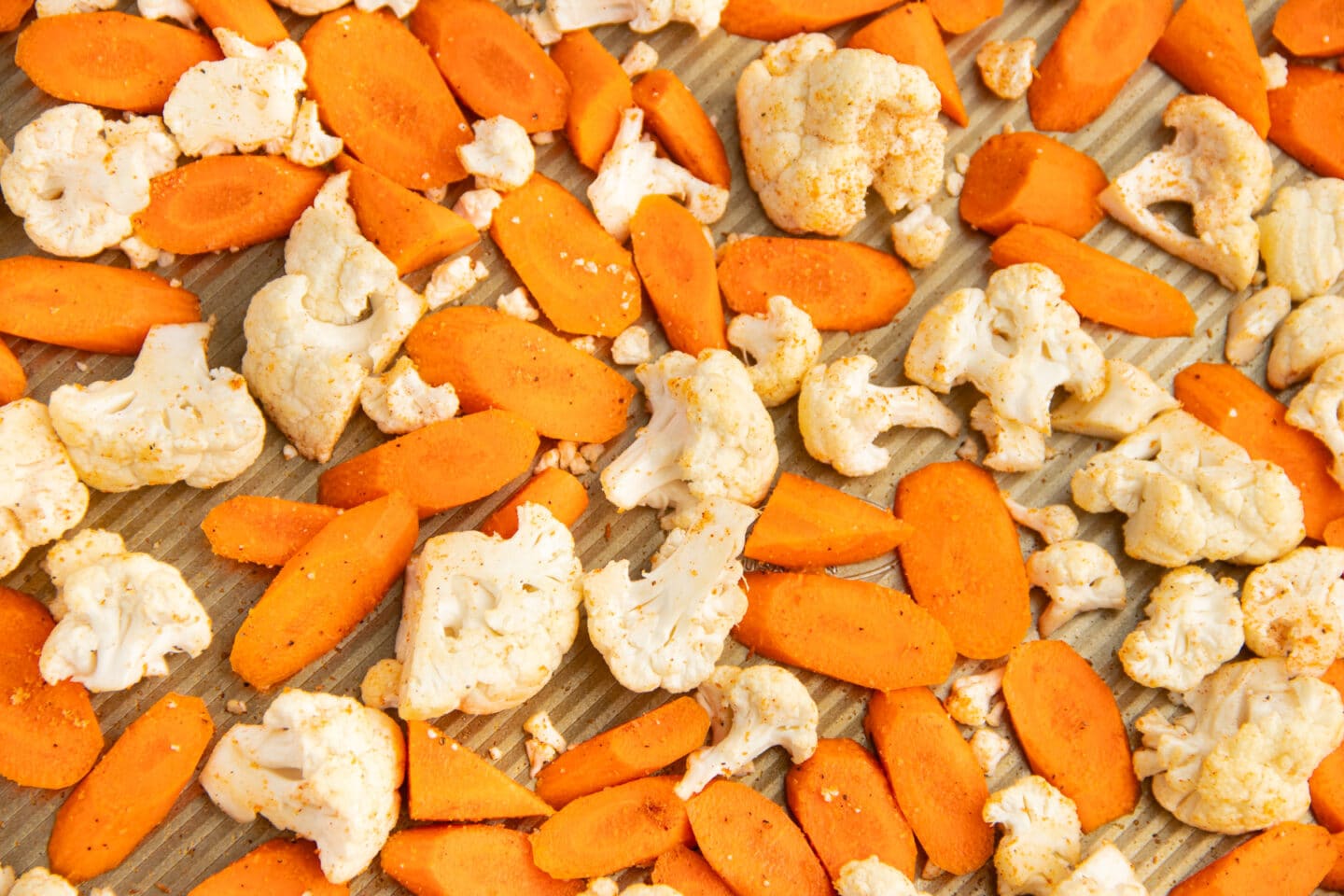 This is a picture of a baking tray with seasoned carrots and cauliflower.