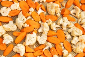 This is a picture of a baking tray with seasoned carrots and cauliflower.