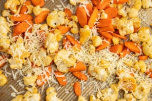 This is a picture of a baking tray with roasted carrots and cauliflower with cheese added.