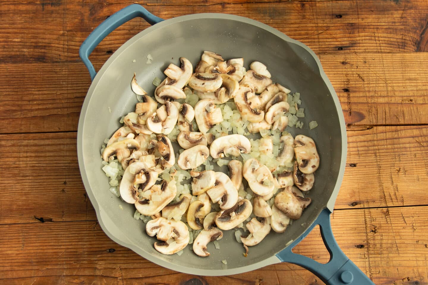This is a picture of a skillet with onion and mushrooms cooking.