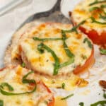 This is a square close-up picture of a baked tomato with melted cheese.