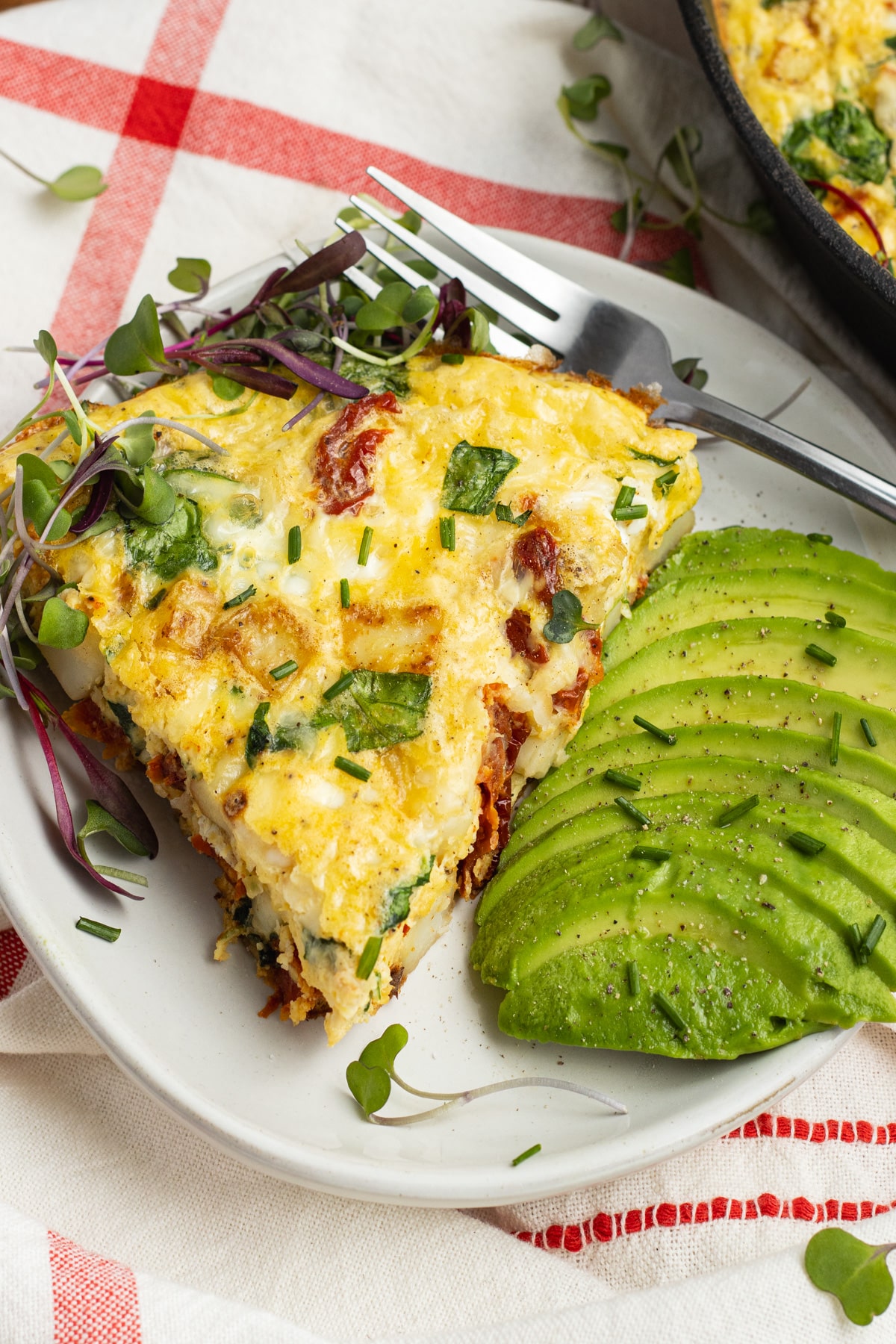 This is a picture of a slice of frittata with avocado on the side.