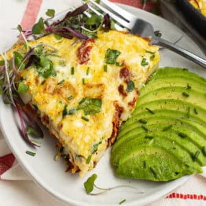 This is a square picture of a slice of frittata with avocado on the side.