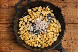 This is a picture of a skillet with cubed potatoes with added shallots.
