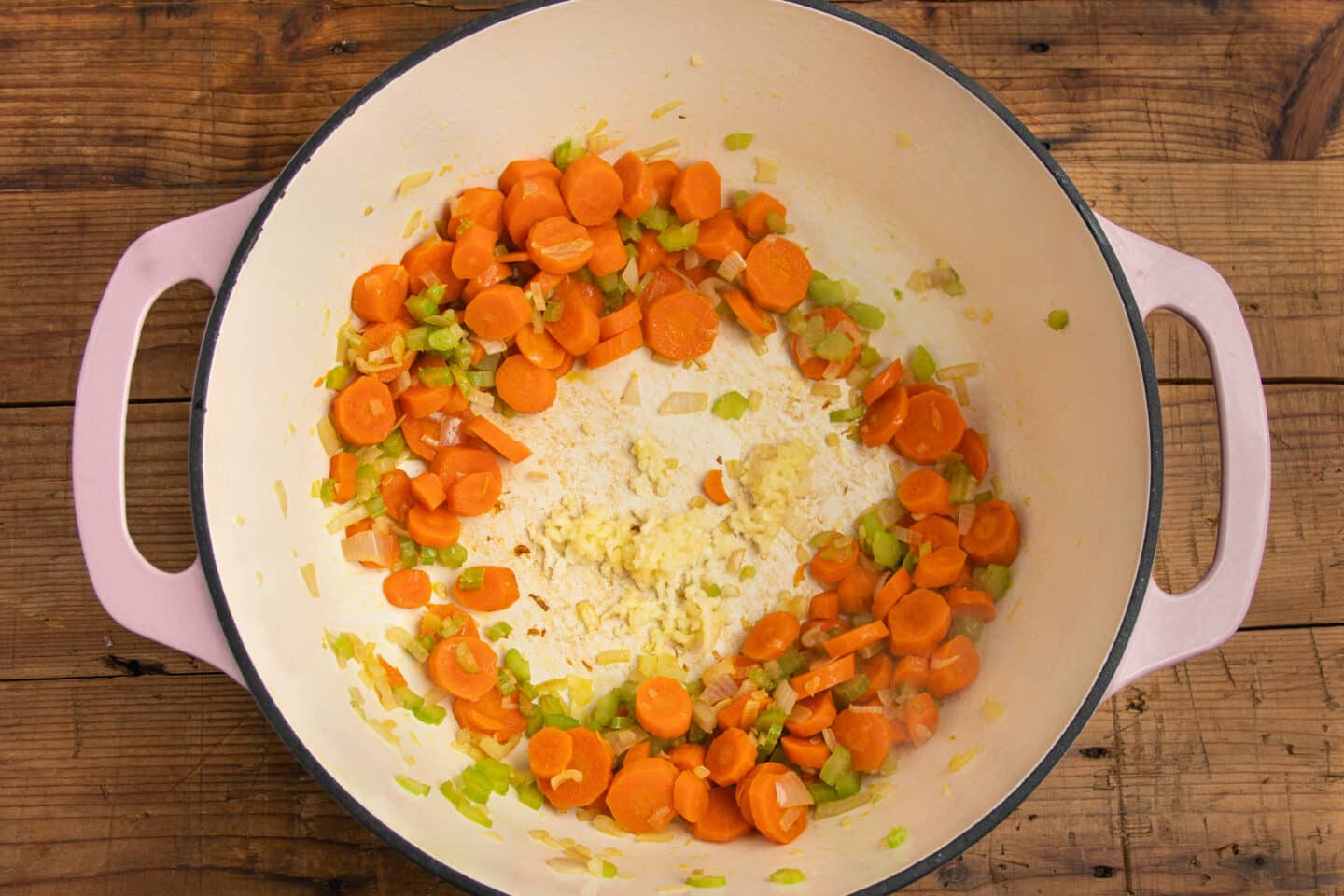 This is a picture of a large pot with carrots, onions and celery with added garlic.