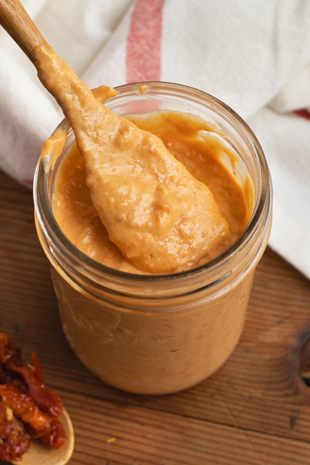 This is a picture of a jar of sun-dried tomato aioli with a spoon.