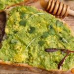 This is a square picture of a close up avocado toast with honey.