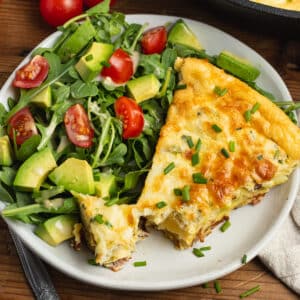 This is a square picture of the frittata on a plate with a side salad.
