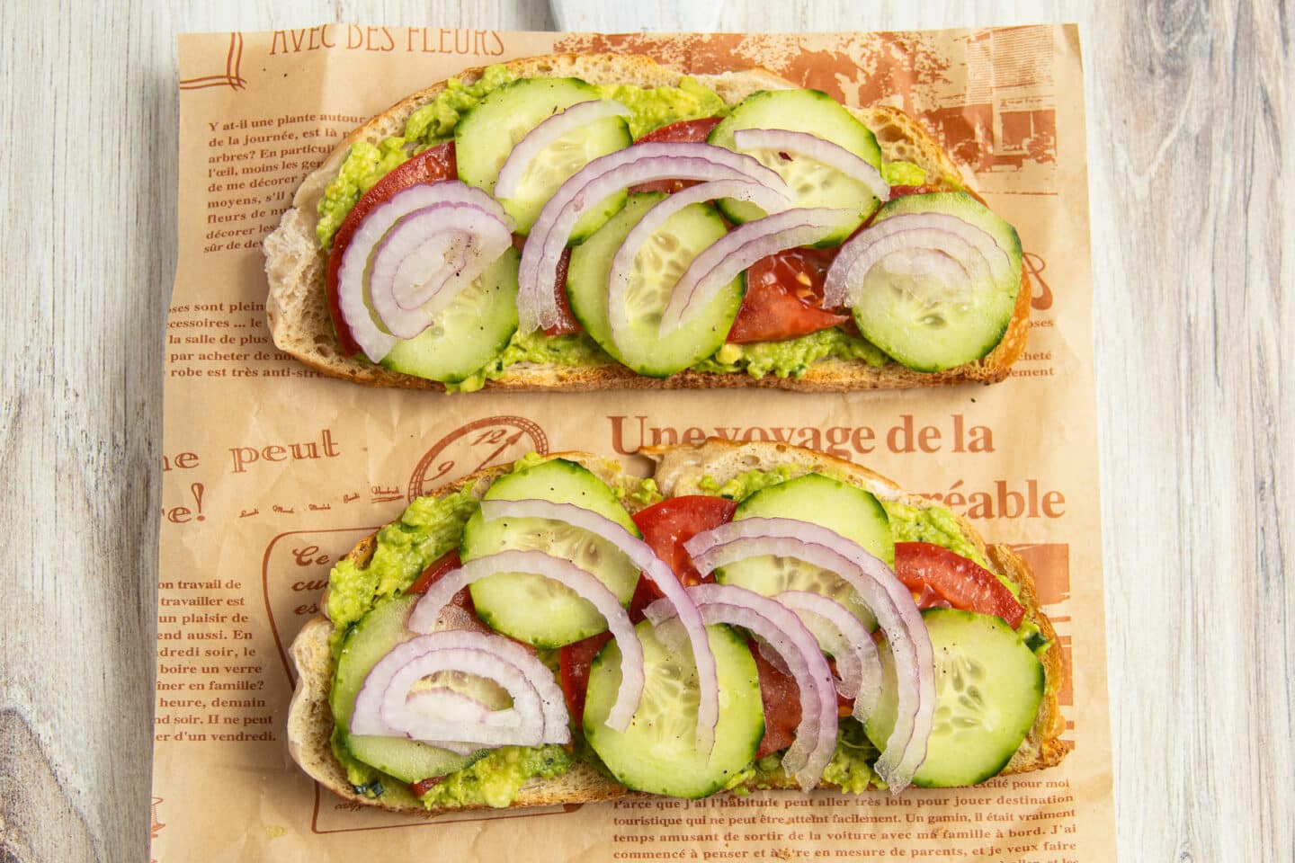 This is a picture of 2 toasts with toppings added to them including cucumber, tomato and onion.