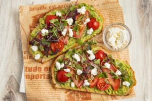 This is a picture of two avocado toasts with tomato, goat cheese and microgreens.