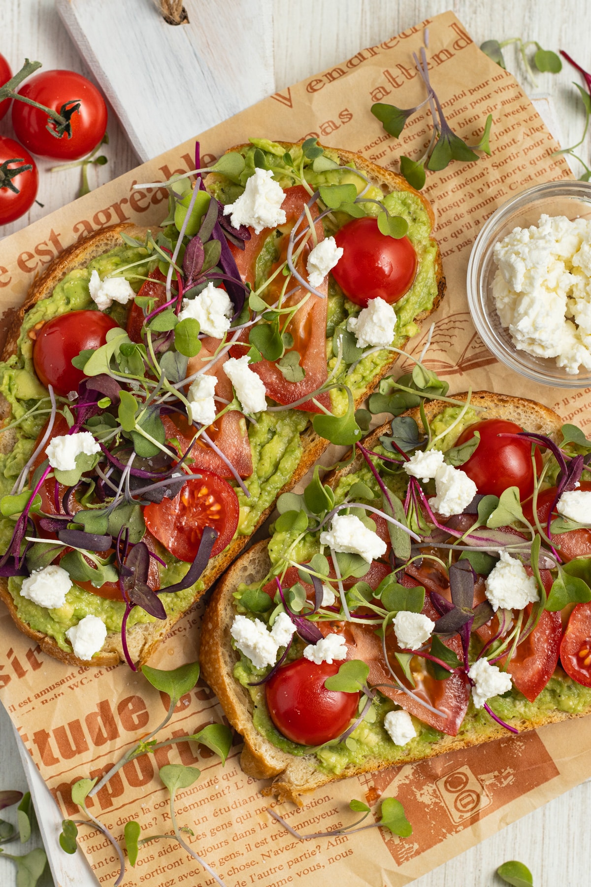 This is a picture of two avocado toasts with tomato, goat cheese and microgreens.