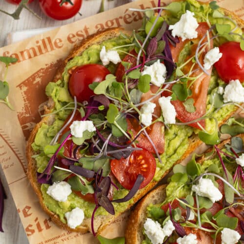 This is a square picture of an avocado toast with tomato and goat cheese.