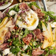 This is a square picture of arugula burrata salad with prosciutto and pear.