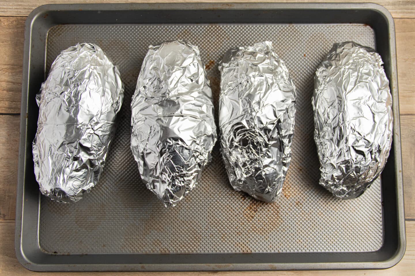 This is a picture of sweet potatoes wrapped in foil on a baking sheet.