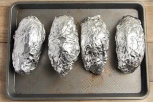 This is a picture of sweet potatoes wrapped in foil on a baking sheet.