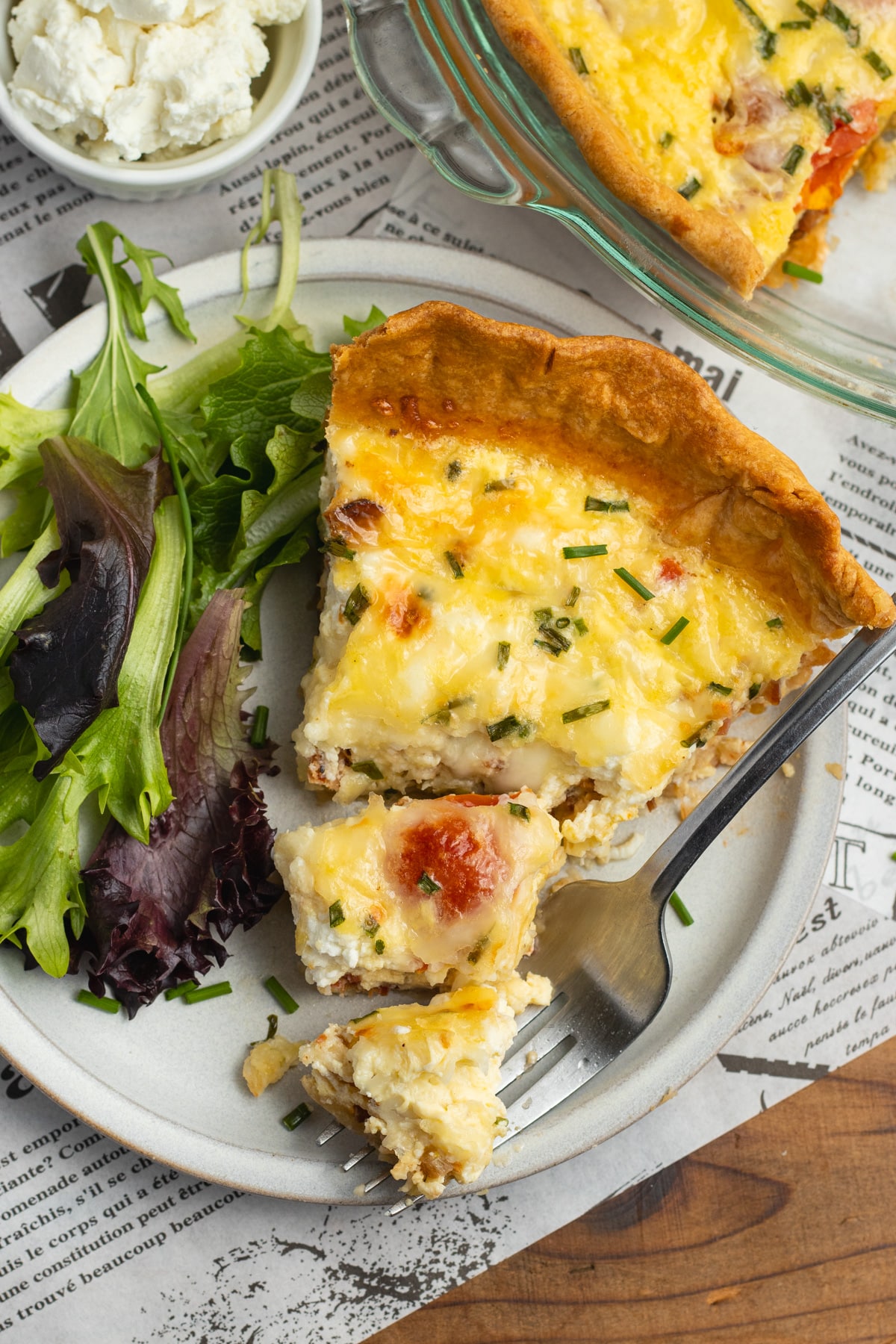This is a picture of a plate with. a slice of tomato bacon goat cheese quiche with gruyere.