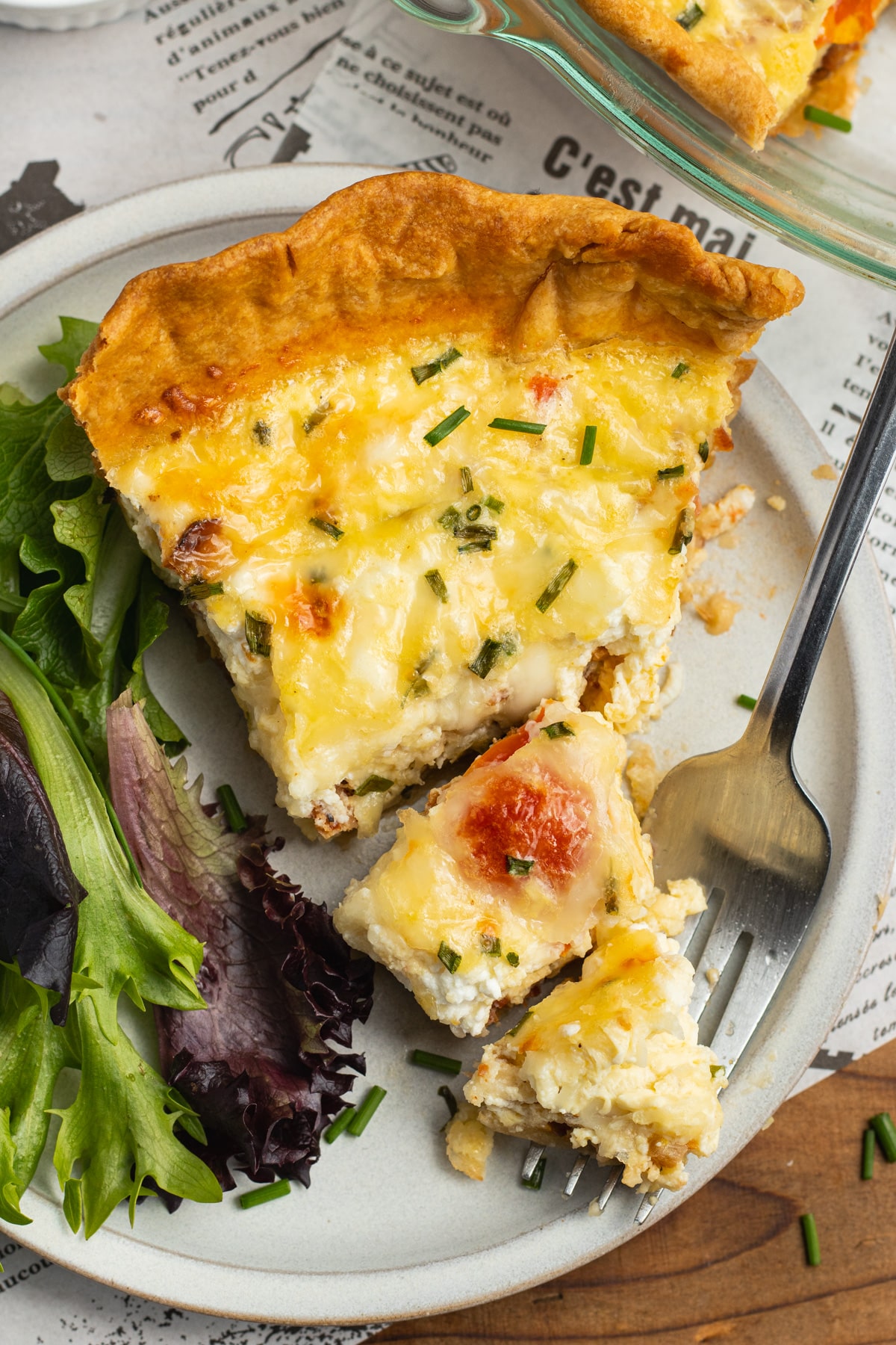 This is a picture of a plate with a slice of tomato bacon goat cheese quiche with gruyere.