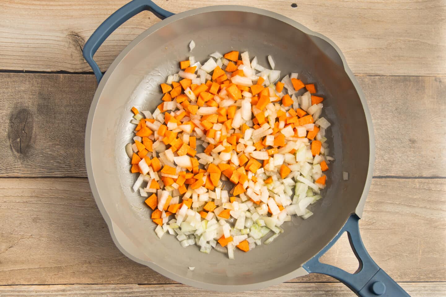 This is a picture of a skillet with onion and carrot cooking.