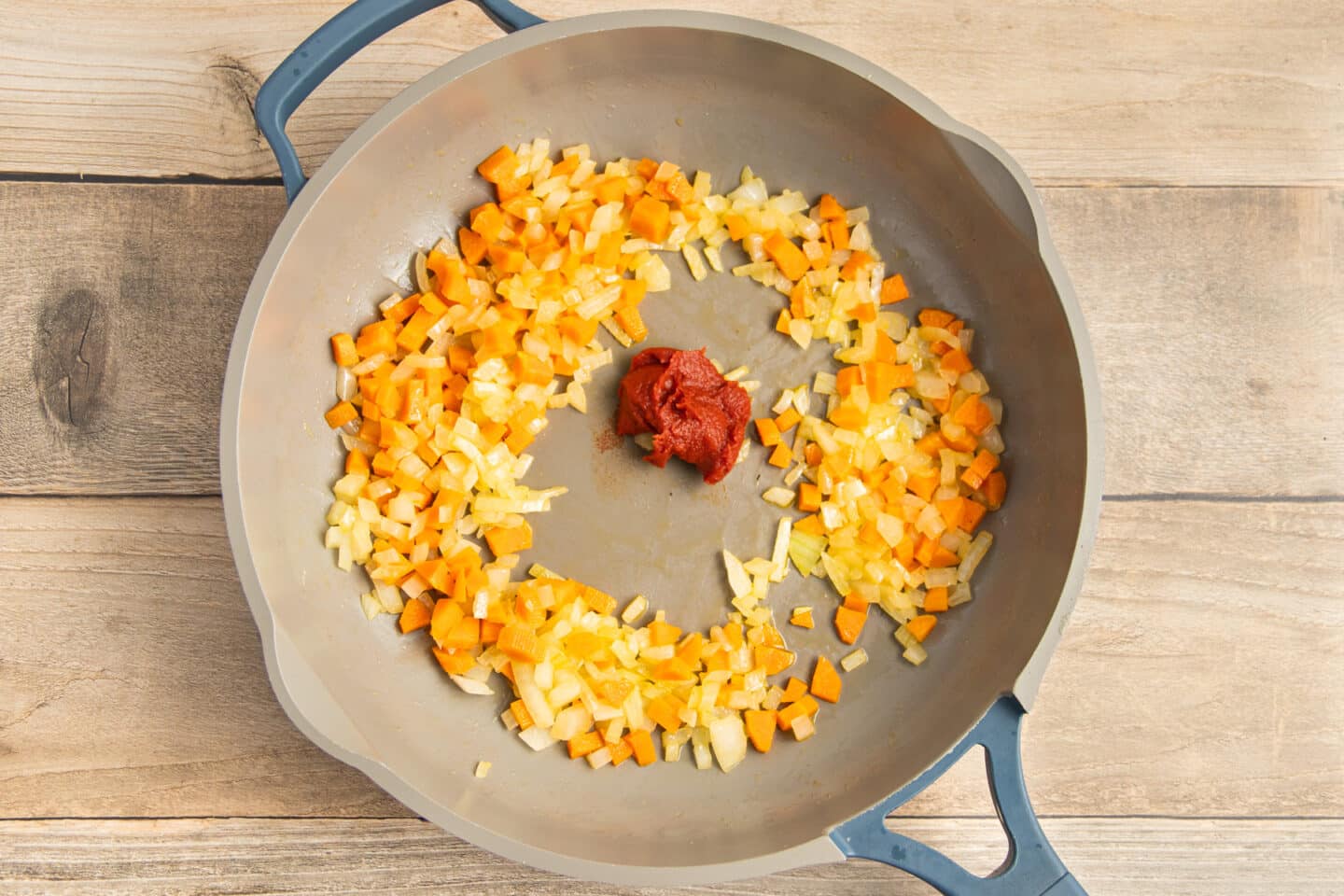 This is a picture of a skillet with onion and carrot cooking and tomato paste added.
