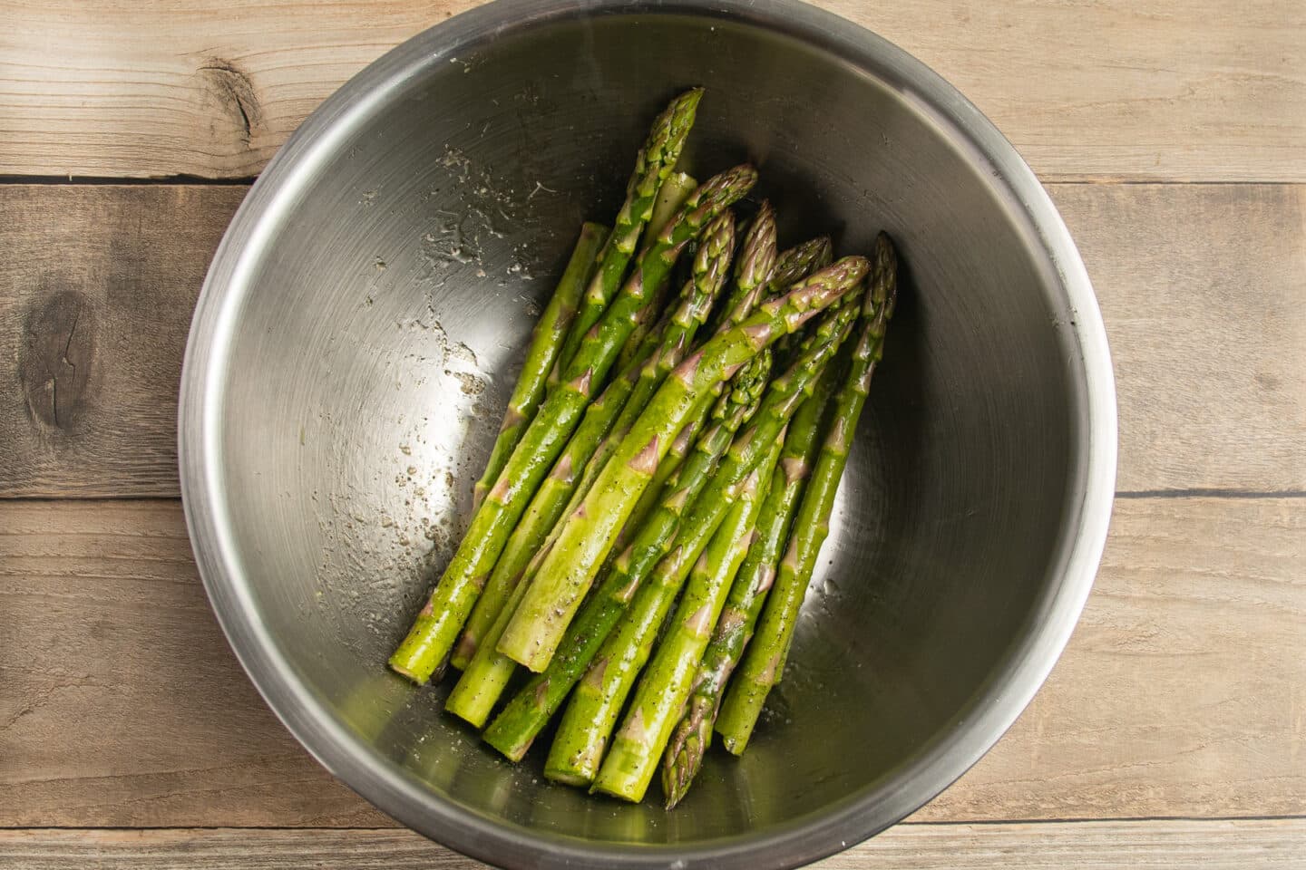 This is a picture of asparagus in a bowl with oil and seasoning.