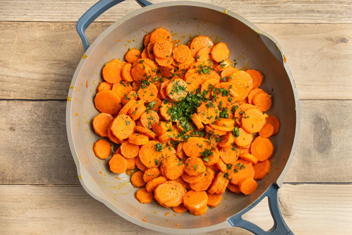 This is a picture of sliced carrots cooking in a skillet with added parsley.